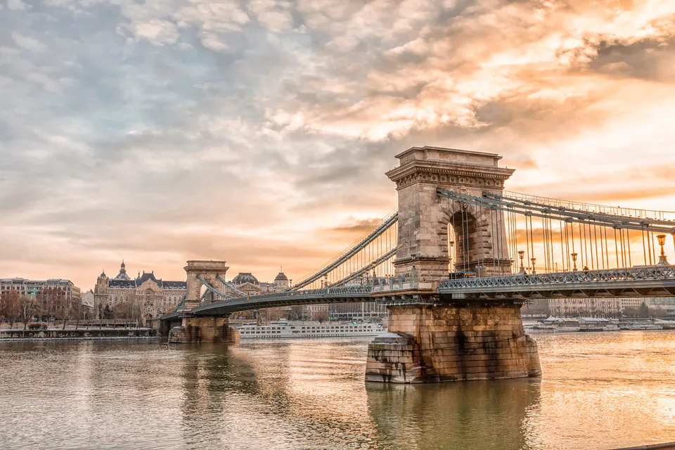 Historic Chain Bridge spans Danube River at sunset with neoclassical towers and golden sky
