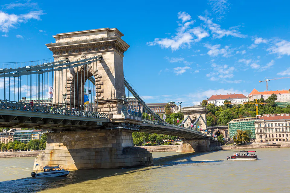 Chain Bridge spanning the Danube River with small boats passing underneath on a sunny day