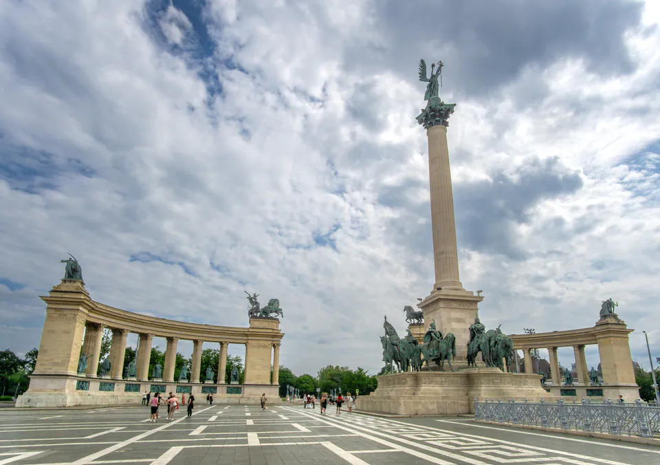 Millennium Monument rises between curved colonnades at Heroes' Square under dramatic cloudy sky