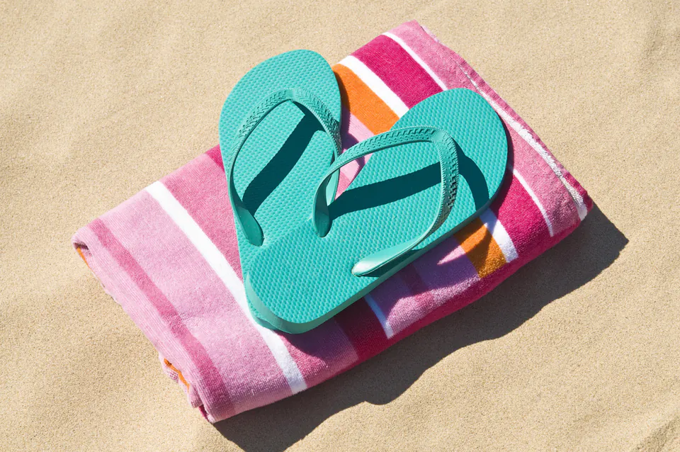 Turquoise flip-flops placed on pink striped towel on sand