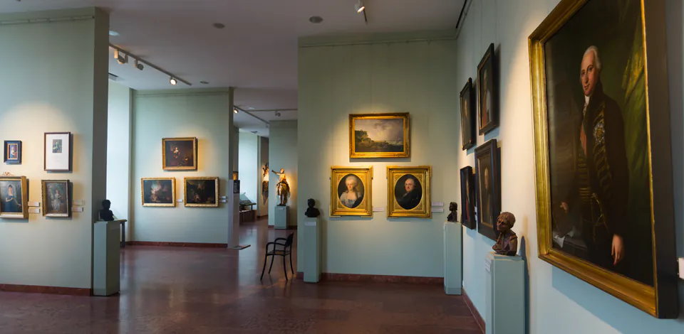 Gallery hall displaying historic portraits and paintings on mint green walls with sculptures on pedestals
