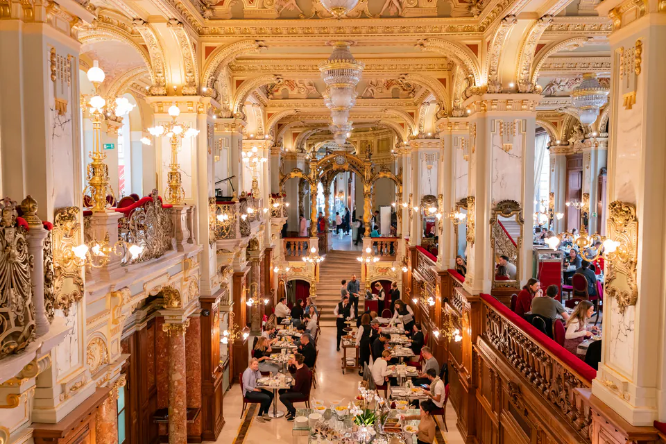 Ornate interior of New York Café with gilded columns, crystal chandeliers and diners at tables
