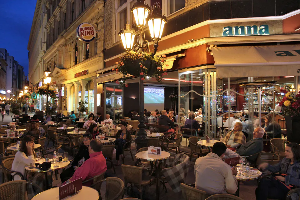 Well-lit street cafe with outdoor seating and patrons dining at night in Budapest