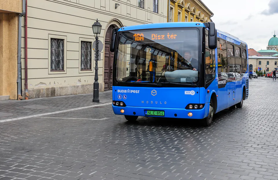 Blue Budapest city bus driving through historic city center with classical architecture