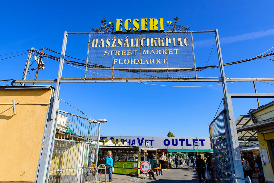 Entrance gate to Ecseri Flea Market with multilingual signage against blue sky