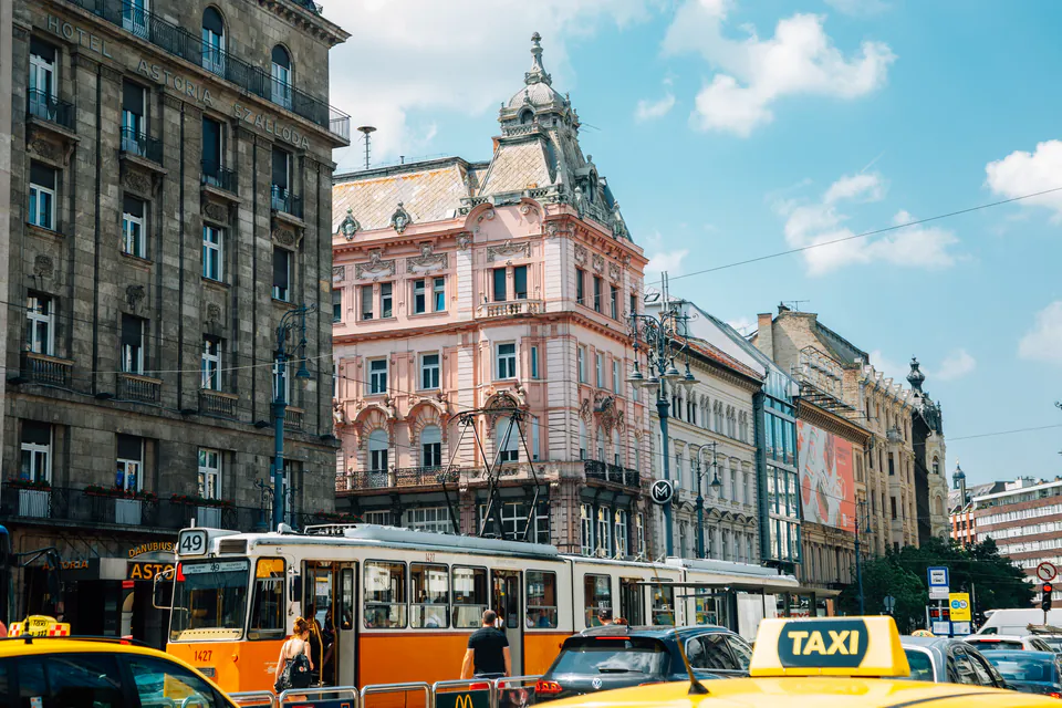Historic Budapest street with ornate buildings, orange tram, and yellow taxis