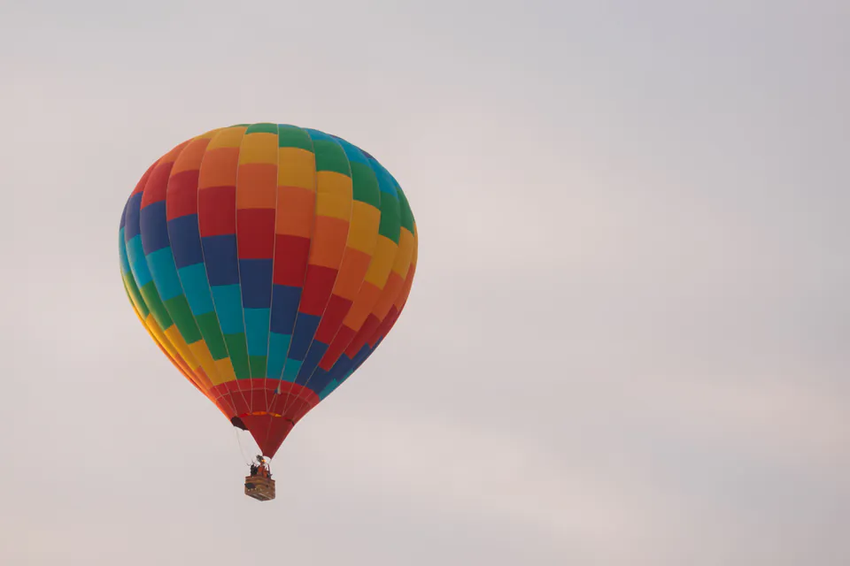 Colorful rainbow-striped hot air balloon floating against cloudy sky