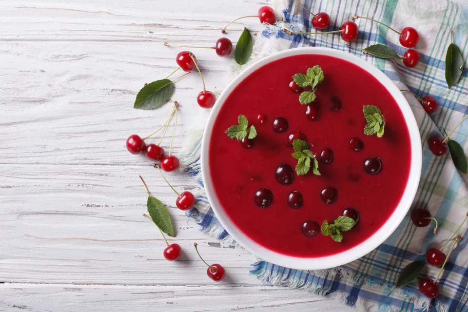 Bowl of bright red sour cherry soup garnished with fresh cherries and mint leaves