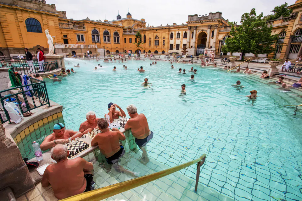 Outdoor thermal pool at Széchenyi Baths with people enjoying chess games in steaming waters