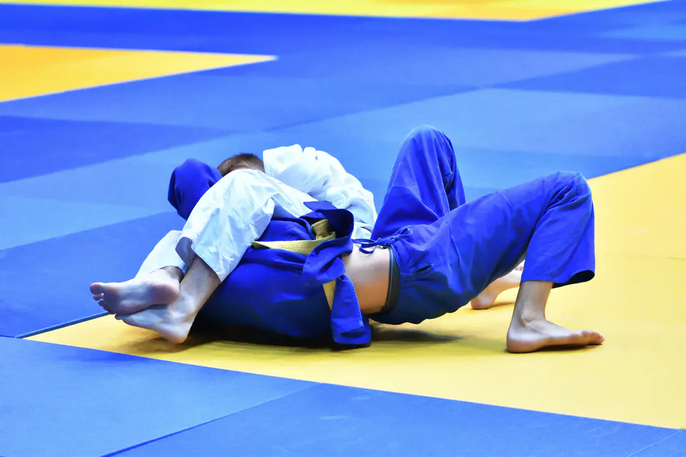 Two judo athletes grappling on blue and yellow mats during competition