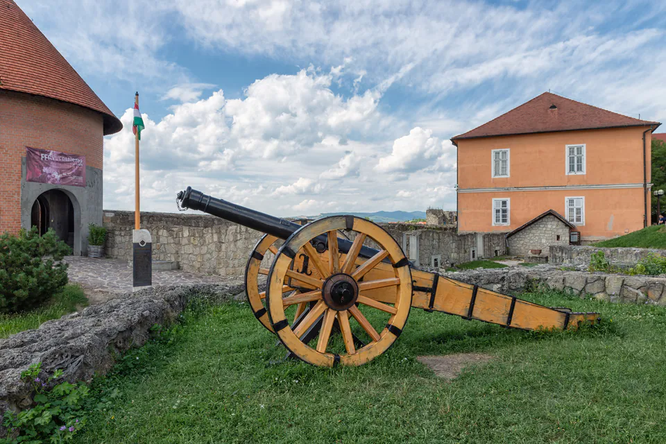 Historic cannon displayed on grass with castle buildings and blue sky in background