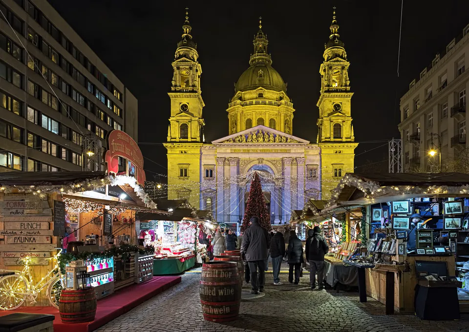 Illuminated St. Stephen's Basilica with Christmas market stalls and shoppers in the foreground