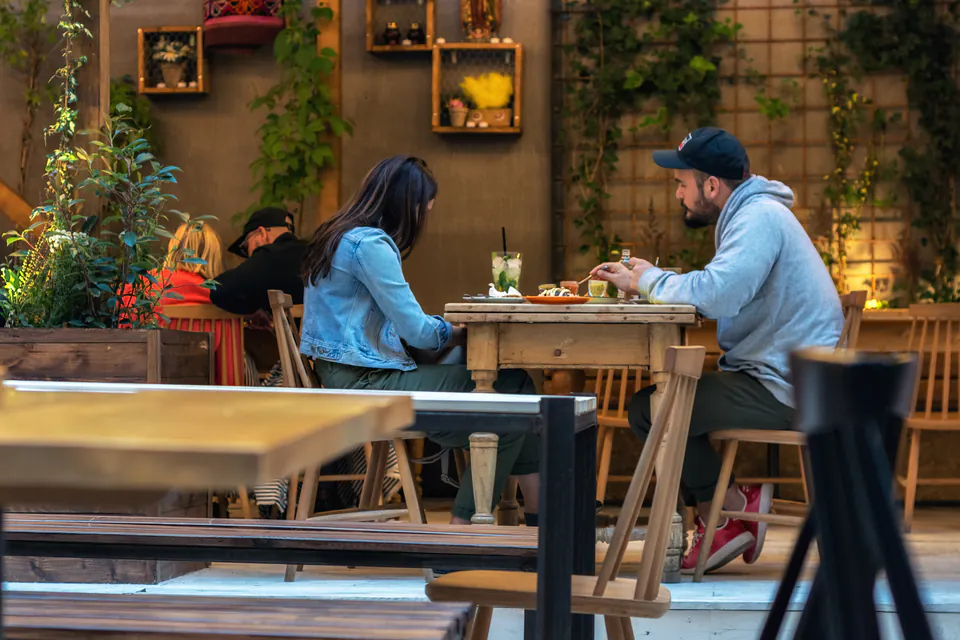 Diners enjoying a meal at wooden tables in a cozy restaurant setting with decorative wall planters