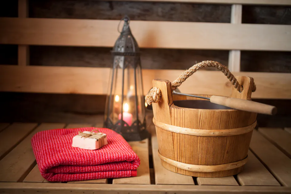 Traditional sauna accessories including wooden bucket, red towels and lantern on wooden bench