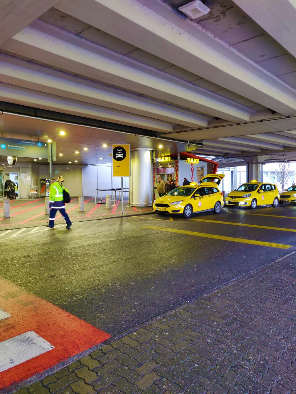 Well-lit airport taxi rank with yellow cabs and security personnel at night