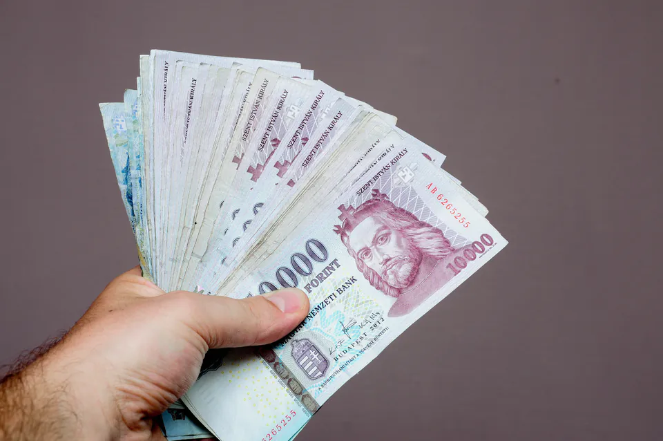 Hand holding a fan of Hungarian Forint banknotes, showing 10000 HUF notes.