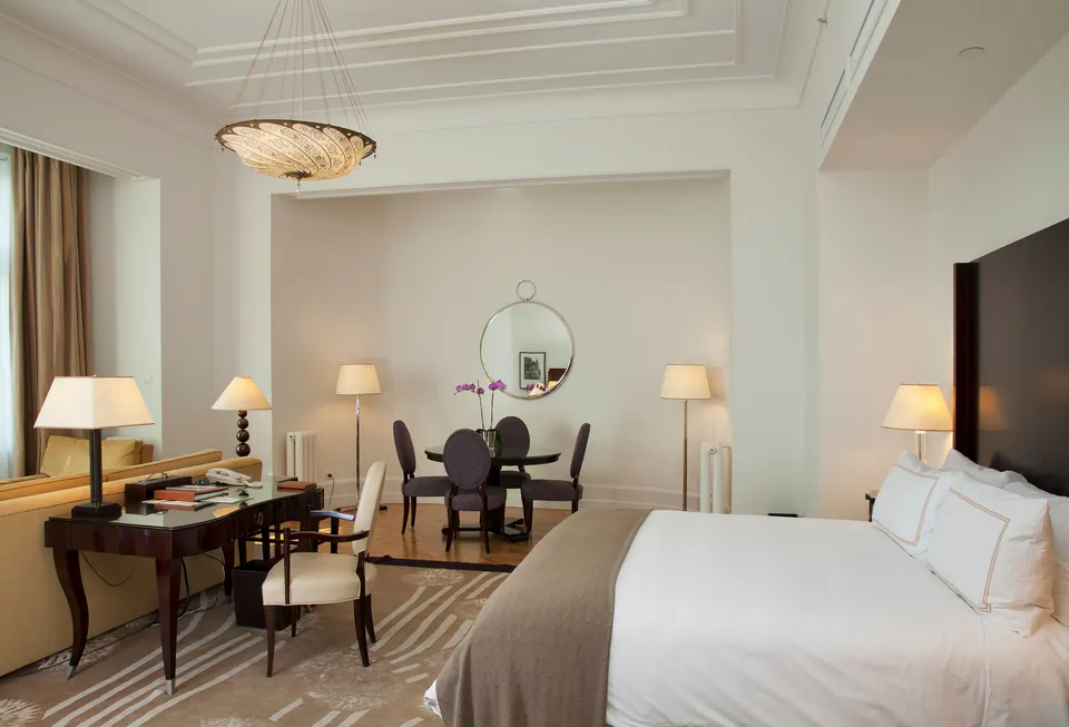 Elegant apartment interior with vintage desk, dining area and modern bed beneath ornate ceiling