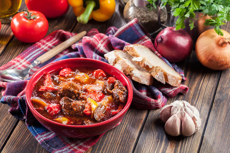 Traditional Hungarian goulash served in red bowl with bread and fresh ingredients