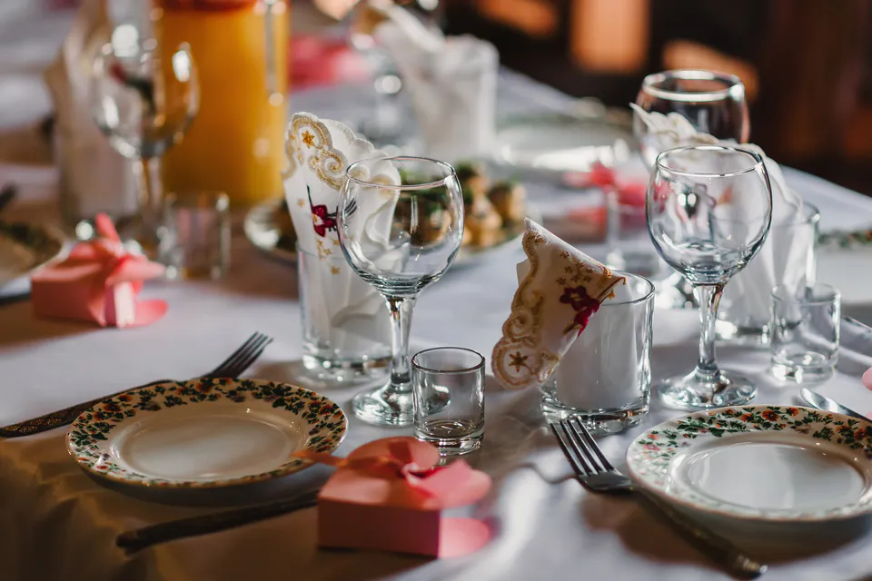 Formal table setting with decorated plates, wine glasses, and folded napkins on white tablecloth