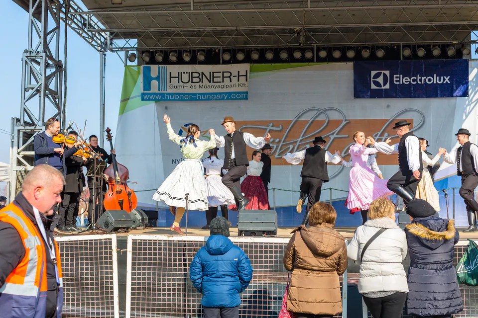 Folk musicians perform with violin and bass while dancers in traditional costumes perform on stage