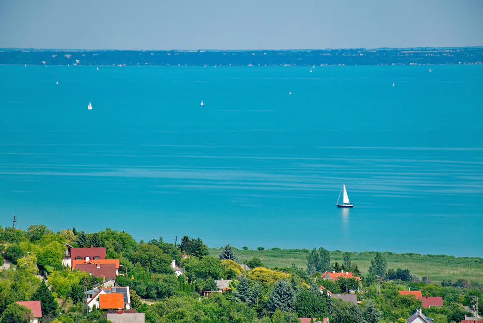 Turquoise waters of Lake Balaton with sailboats and colorful houses along green hillside