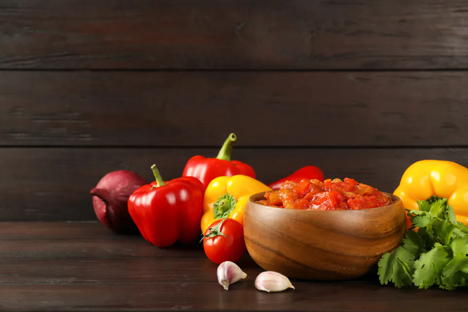 Fresh vegetables and ingredients including peppers, tomatoes, garlic and herbs on dark wooden surface