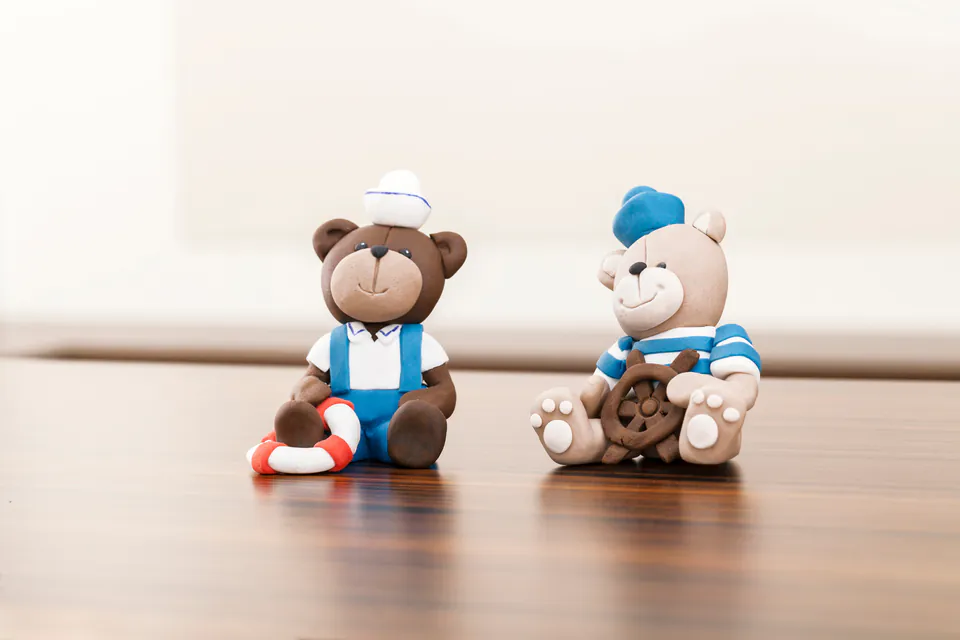 Two decorative marzipan teddy bears displayed on wooden surface, wearing sailor and casual outfits