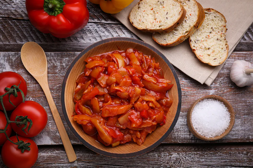 Bowl of sautéed red peppers with tomatoes and bread on rustic wooden table