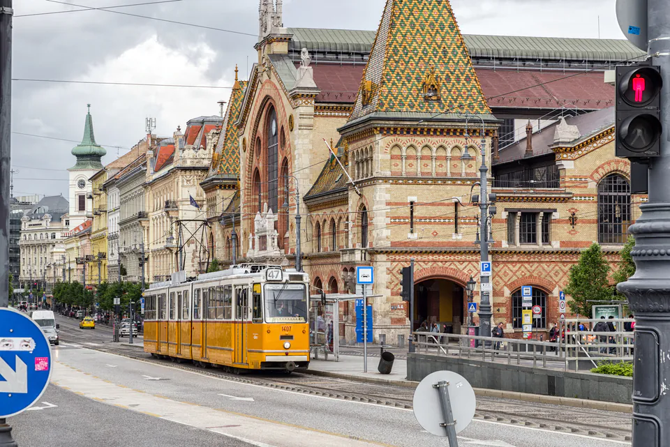 Yellow tram passing in front of the Great Market Hall with its ornate neo-Gothic facade