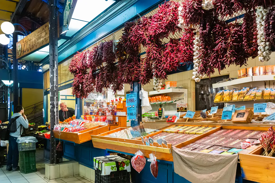 Market stall with dried red paprika peppers hanging above spice displays and packaged goods