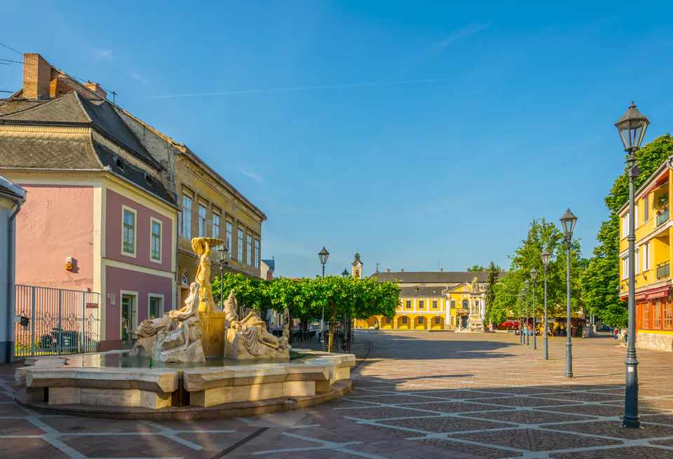 Historic Széchenyi Square with ornate fountain and pastel-colored baroque buildings in morning light