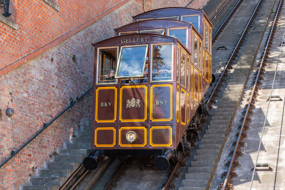 Historic funicular railway car ascending steep tracks along brick wall to Buda Castle