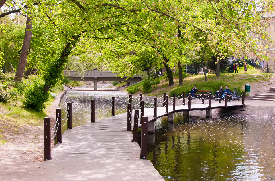 Curved wooden boardwalk over pond with green trees and bridges in City Park Budapest
