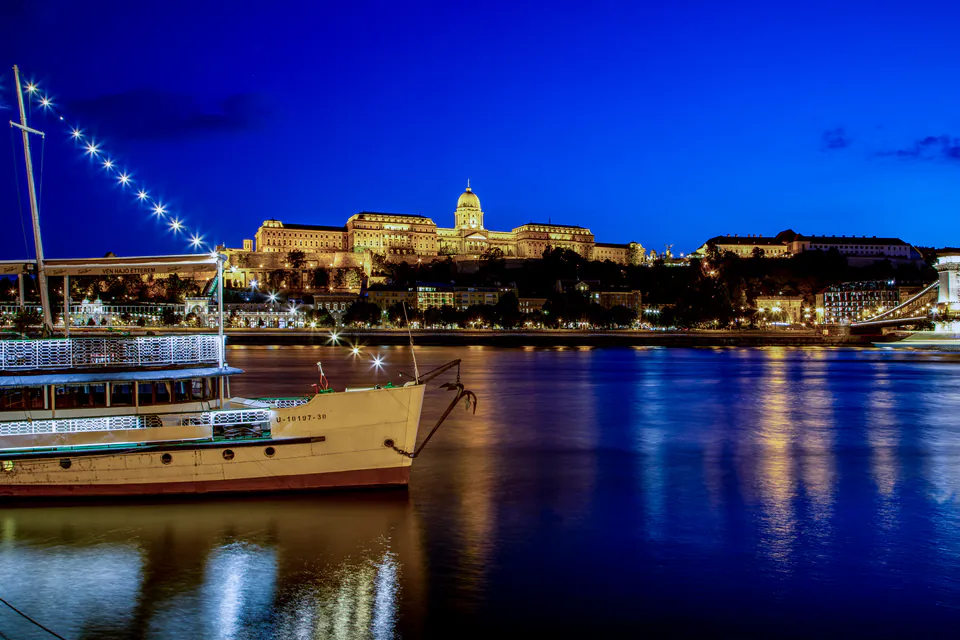 Evening view of illuminated Buda Castle with moored boat on Danube River