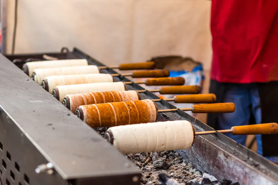 Fresh chimney cakes cooking on rotating spits over hot coals at a street vendor