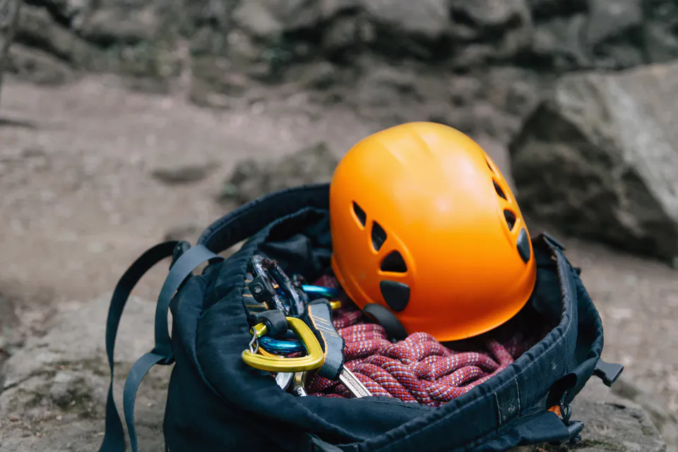 Safety equipment including orange climbing helmet, ropes and carabiners in backpack