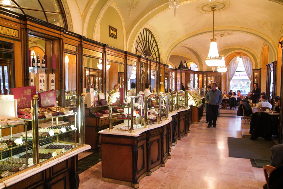 Historic interior of Café Gerbeaud showing ornate display cases filled with pastries under vaulted ceilings