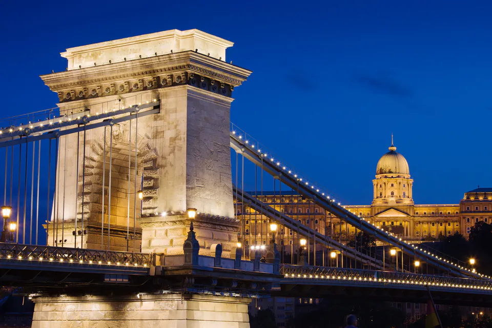 Historic stone tower of Chain Bridge illuminated at night with Buda Castle in background