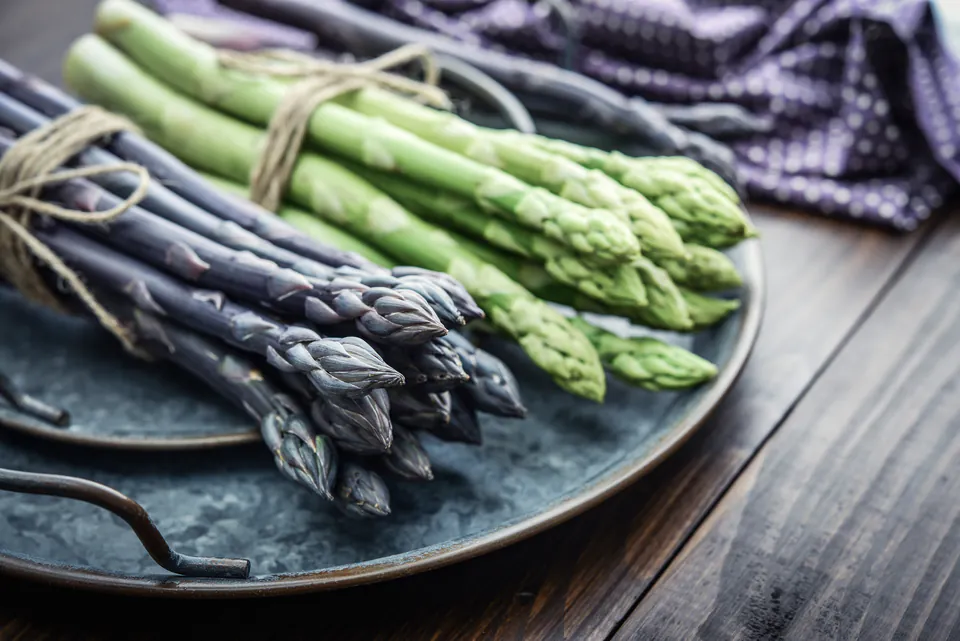 Fresh green and purple asparagus bundles arranged on a dark ceramic plate