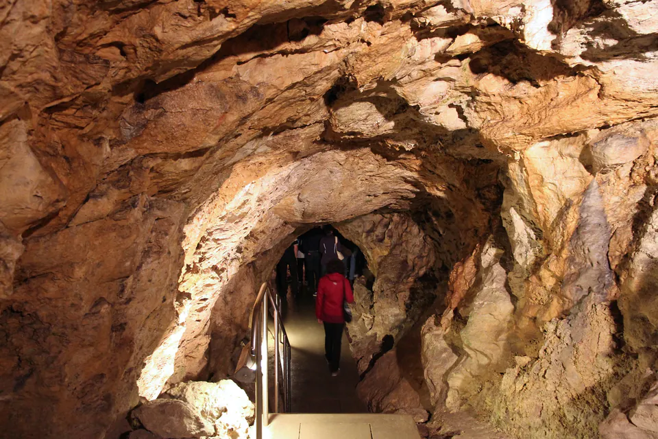 Illuminated cave passage with handrails showing visitors exploring underground tunnel system