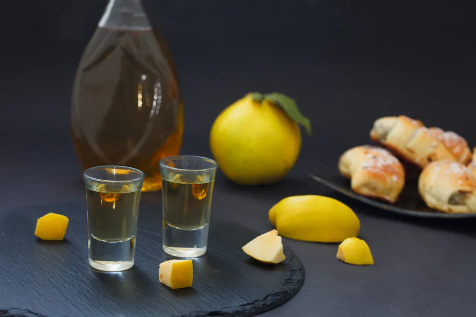Shot glasses of clear spirit with lemons and pastries on dark slate surface