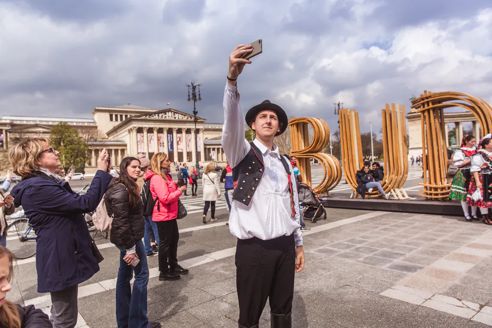Performer in traditional Hungarian dress taking selfie with tourists at outdoor festival