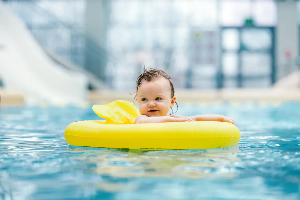 Small child floating in pool with yellow swim ring at indoor waterpark