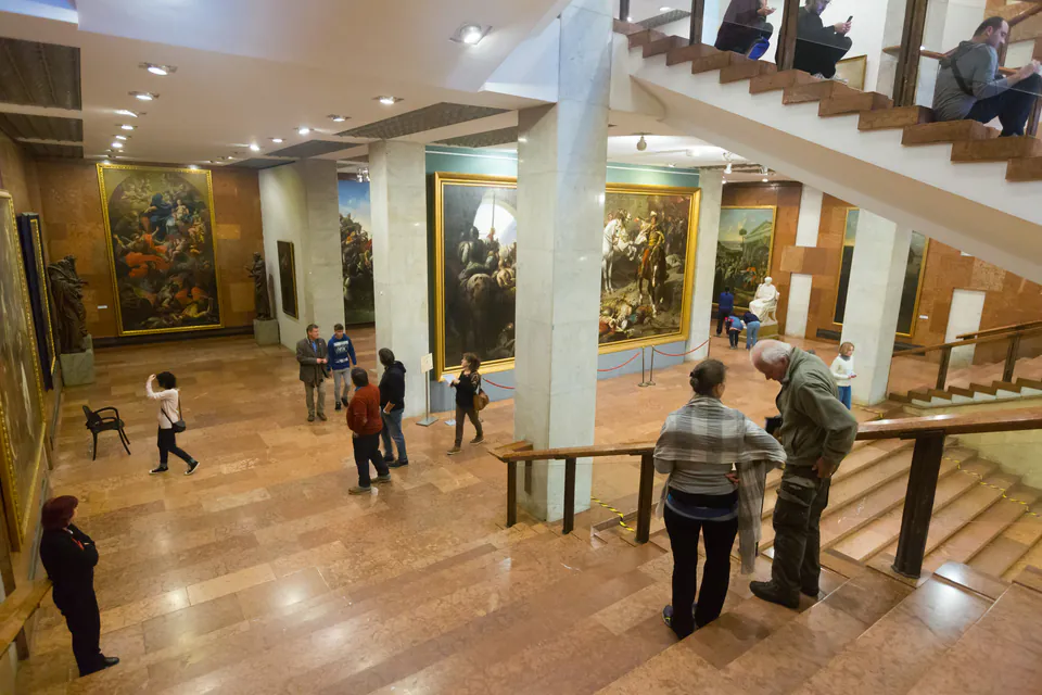 Museum gallery interior with visitors viewing large paintings and using audio guides