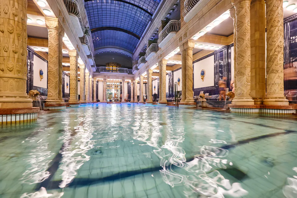 Interior view of an elegant thermal bath hall with ornate columns and glass ceiling
