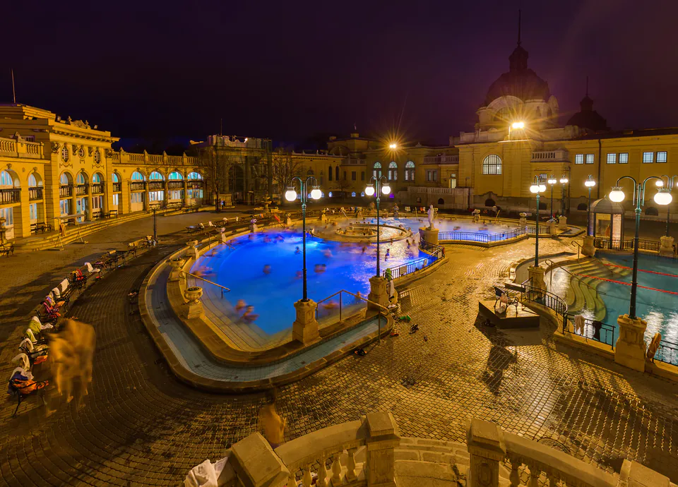 Illuminated outdoor thermal pools at night with blue lighting and neo-baroque architecture