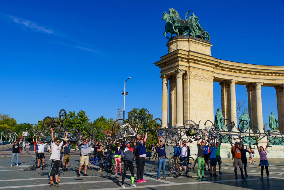 Group of cyclists holding bikes aloft at Heroes Square during guided bike tour
