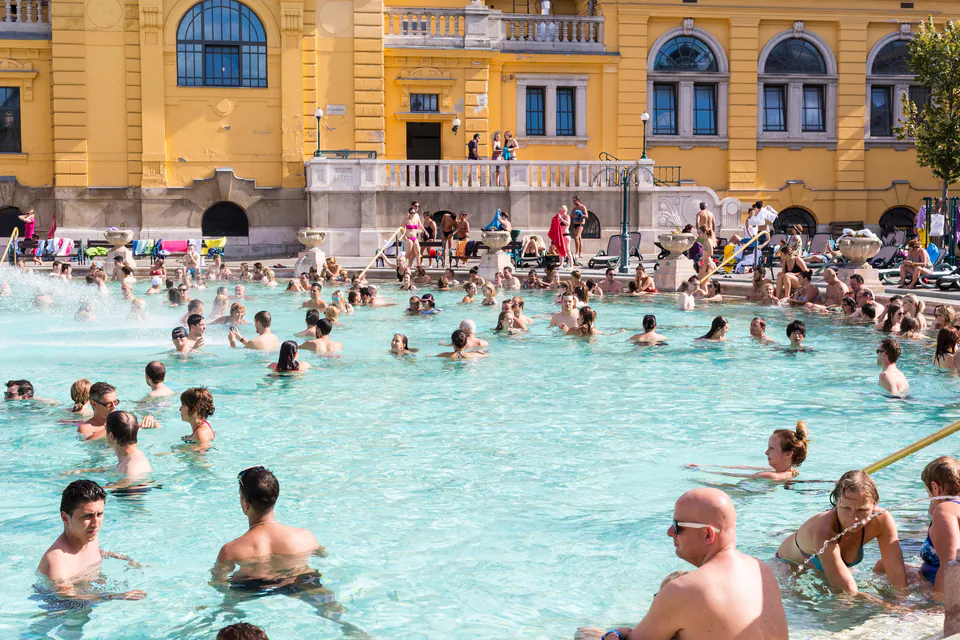 Outdoor thermal pool filled with bathers against neo-baroque yellow building facade