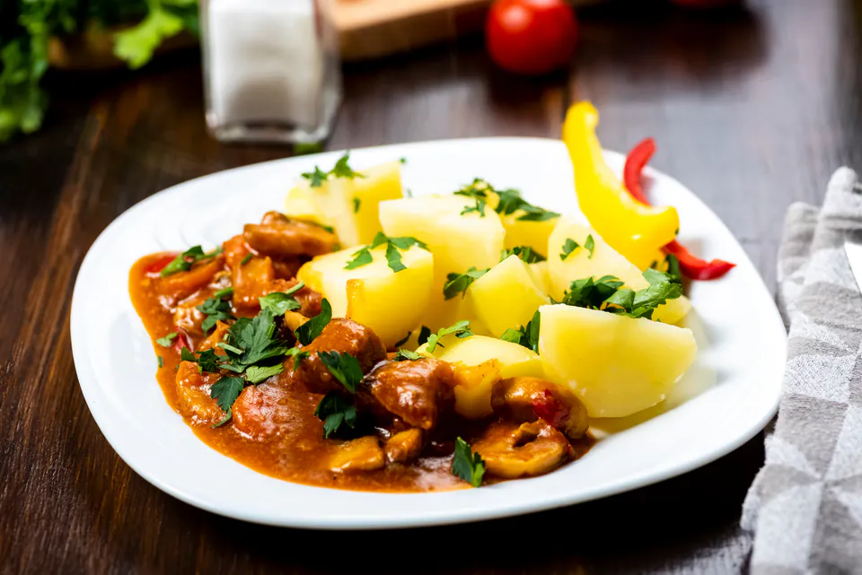 Traditional Hungarian goulash served with boiled potatoes and bell peppers on a white plate