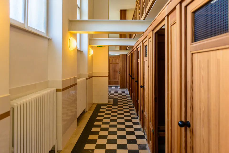Checkered floor hallway with wooden changing cabins and lockers in thermal bath facility